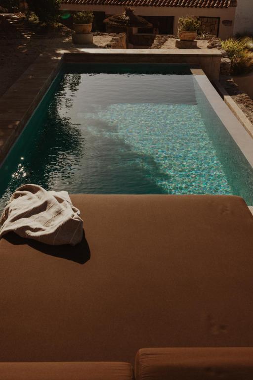 11 UNIQUE Boutique Hotels in Tenerife 8 A rectangular swimming pool with clear blue water, bordered by stone tiles, sits outdoors at one of the charming boutique hotels in Tenerife. In the foreground, a brown lounge chair with a white towel is bathed in warm sunlight.