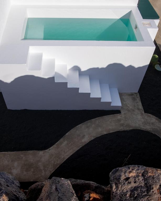 Unique Adults Only Hotels in Lanzarote 12 White stairs lead to a rectangular pool within a stark white structure, casting sharp shadows. Below, a curved concrete path crosses dark gravel—an oasis typical of Adults Only Hotels in Lanzarote.