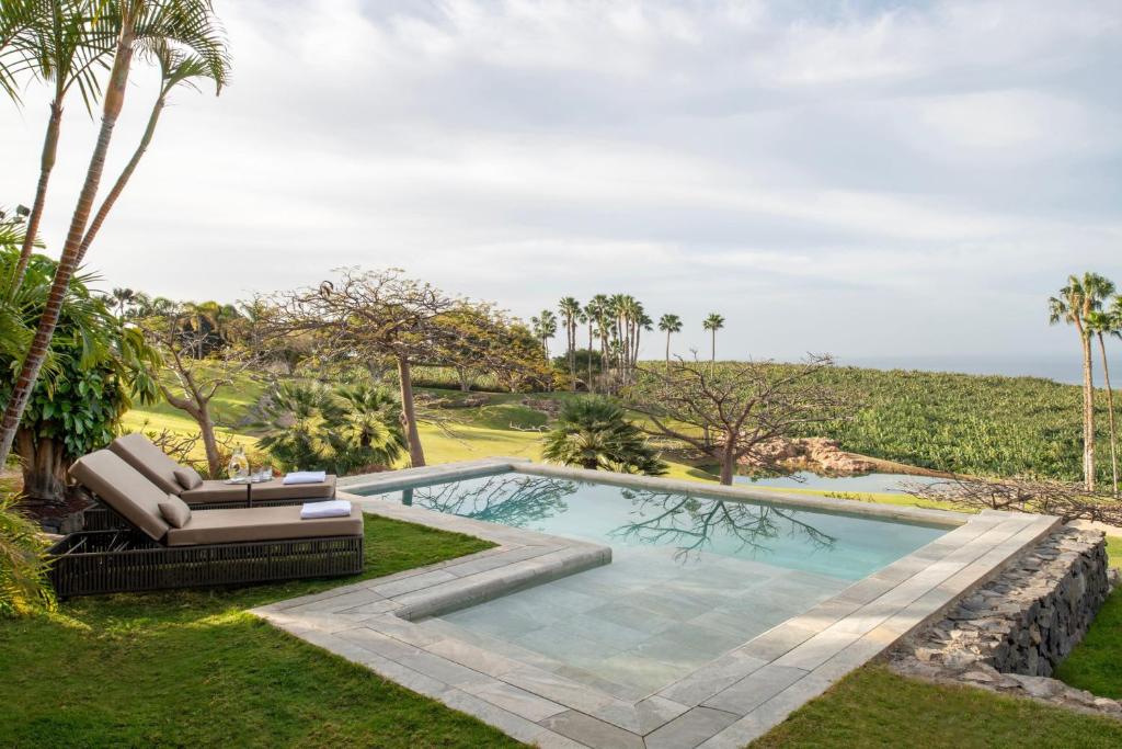 11 UNIQUE Boutique Hotels in Tenerife 45 A serene infinity pool with a sunbed overlooks a lush, green landscape dotted with palm trees and fields under a cloudy sky, capturing the peaceful and relaxing vibe often found at boutique hotels in Tenerife.