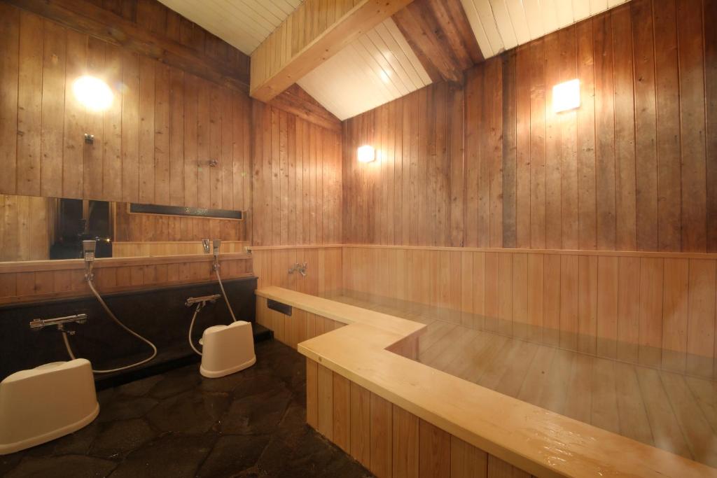 Looking for the Best Ryokan in Takayama? 5 A traditional Japanese wooden bathhouse interior at one of the best ryokan in Takayama, featuring a large rectangular hot tub, two shower stations with stools and mirrors, and warm lighting that creates a cozy atmosphere.