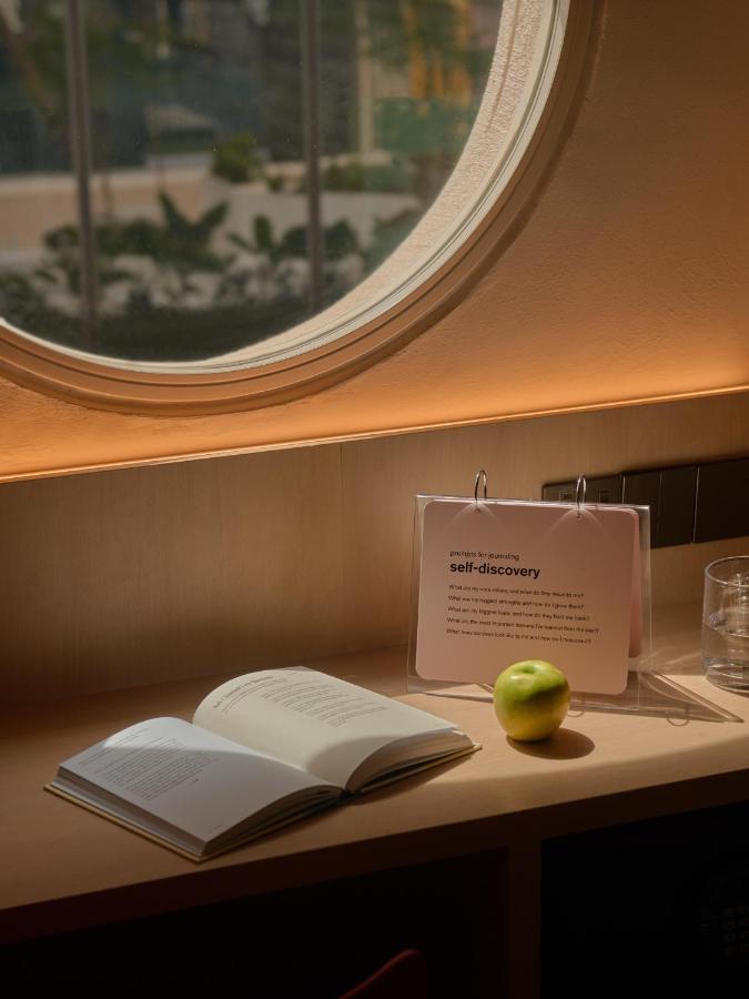13 Most Unique Hotels in Singapore for an Incredible Holiday 39 A sunlit desk under a round window holds an open book, a green apple, and a flip book titled self-discovery—evoking the cozy charm found in unique hotels in Singapore. Soft natural light creates a warm, inviting atmosphere.