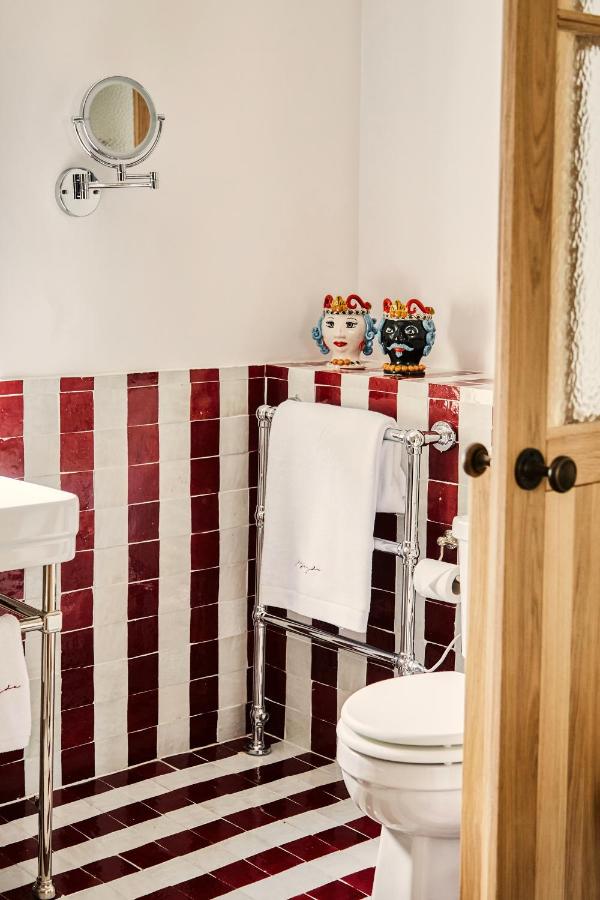 15 Best Boutique Hotels in London, UK 7 A small bathroom reminiscent of the best boutique hotels London offers, featuring red and white vertical striped tiles, a white sink, towel rack with white towels, decorative ceramic jars, and a partially open wooden door.