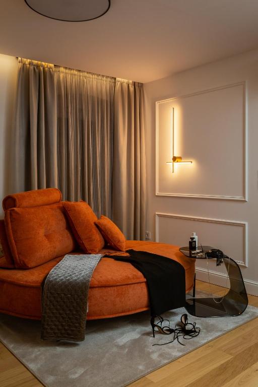 Where to Stay in Split: Hotel & Areas Guide 24 A modern cozy room—perfect for those wondering where to stay in Split—with an orange round sofa, plush pillows, a gray blanket, and a black dress draped over it. A glass side table holds drinks; black heels rest nearby, softened by warm lighting and gray curtains.