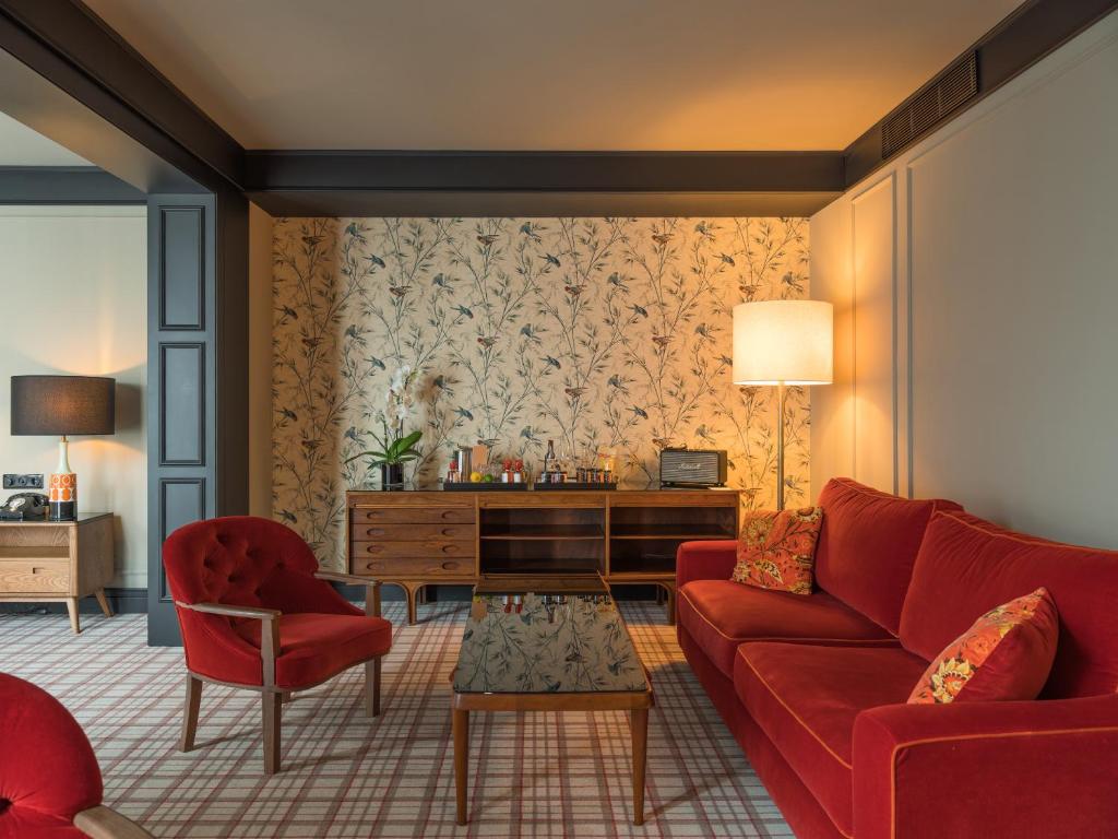 Top Barcelona Hotels with Rooftop Pool 45 A living room with red velvet sofa and armchair, glass coffee table, wooden sideboard, floral wallpaper, and a tall floor lamp evokes the cozy charm of Barcelona Hotels with Rooftop Pool in a mid-century modern atmosphere.