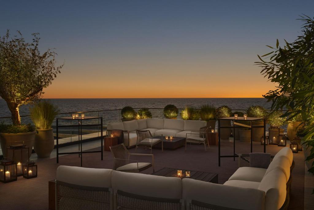 9 Best Hotels in Saudi Arabia: Unique Stays Across the Country 7 A cozy outdoor patio at one of the Best Hotels in Saudi Arabia features white cushioned sofas and small tables, softly lit by lanterns, overlooking the ocean at sunset with a clear sky and lush potted plants around the seating area.