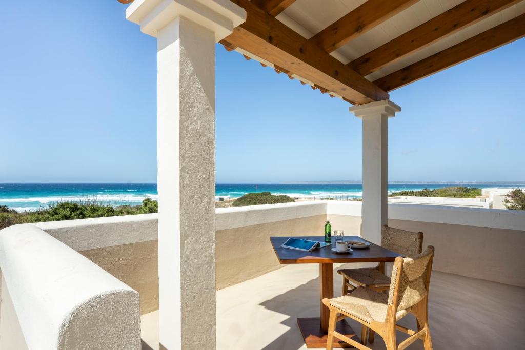 A covered terrace at one of the boutique hotels in Formentera features two chairs and a table set for breakfast, overlooking the bright blue ocean and sandy beach under a clear sky.