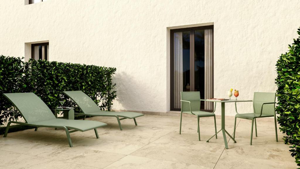 A patio at one of the boutique hotels in Asturias, featuring two lounge chairs, a round table with drinks, and a charming white wall with doors, all nestled among lush green hedges.