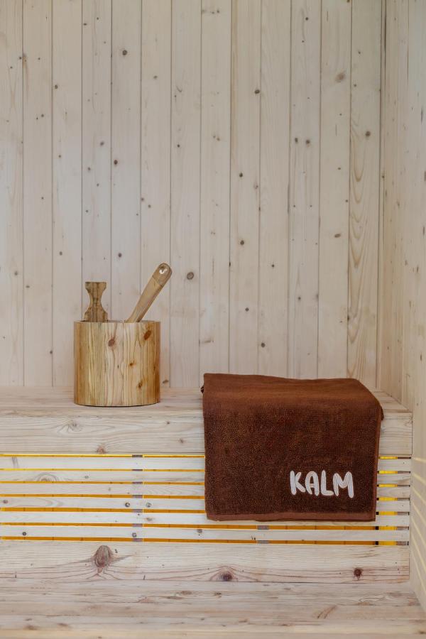 14 UNIQUE Boutique Hotels in Canggu, Bali 37 A wooden sauna interior with a brown towel labeled KALM on the bench and a wooden bucket and ladle set beside it, evoking the serene ambiance found in boutique hotels in Canggu.
