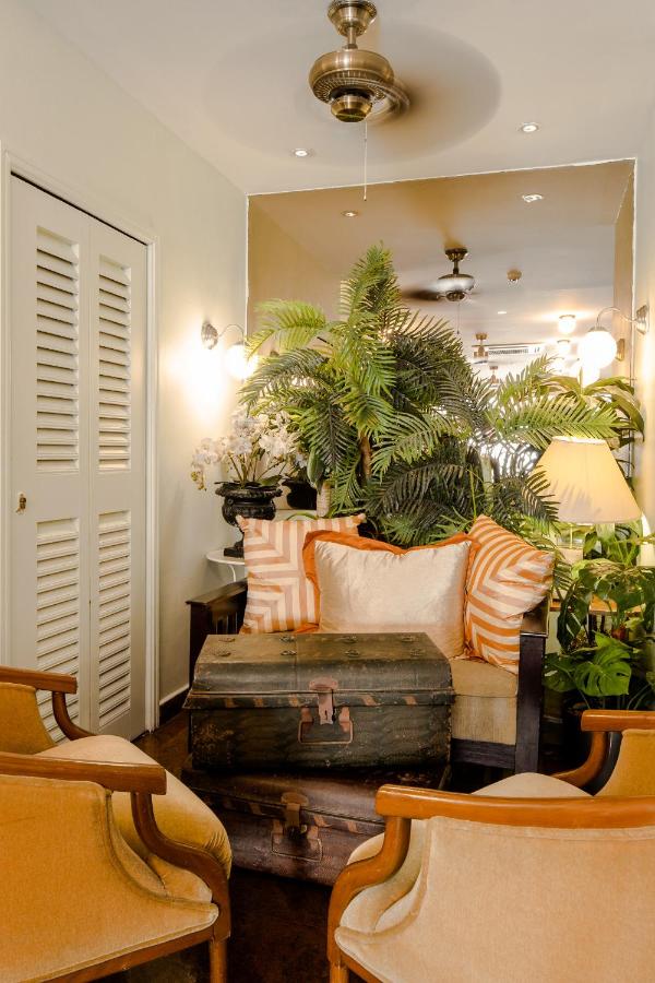 13 Most Unique Hotels in Singapore for an Incredible Holiday 47 A cozy living room with beige armchairs and a wooden bench with striped pillows, a vintage trunk as a coffee table, lush green plants, and warm lighting—reminiscent of the inviting interiors found in unique hotels in Singapore.