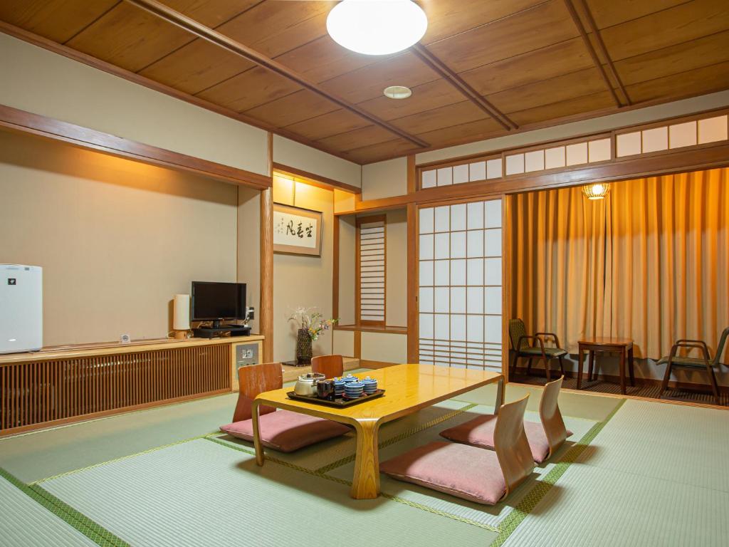 8 BEST Ryokans in Osaka 22 A traditional Japanese tatami room inspired by ryokans in Osaka, with a low wooden table, floor cushions, sliding shoji doors, and a small sitting area by the window. Warm lighting, minimal decor, and wooden ceiling panels complete the space.