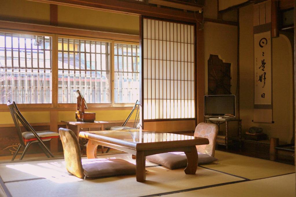 Looking for the Best Ryokan in Takayama? 21 A traditional Japanese room at the Best Ryokan in Takayama features tatami mats, a low wooden table, floor cushions, sliding shoji doors, a small TV, and sunlight streaming through wooden lattice windows with elegant decor and calligraphy.
