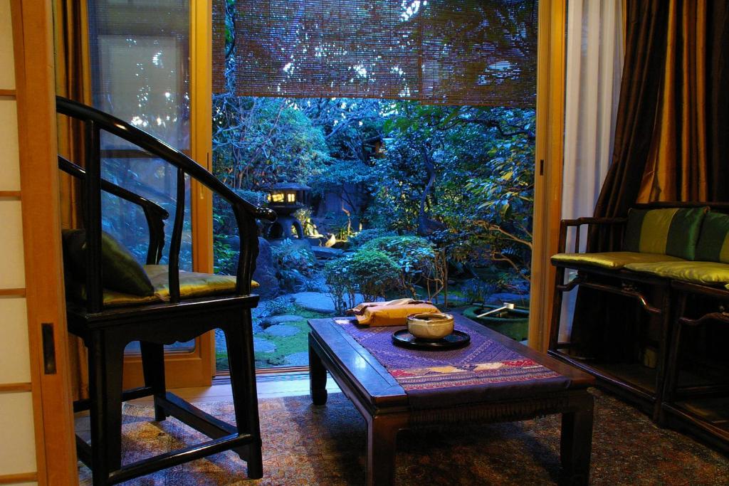 7 UNIQUE Ryokans in Gion Kyoto 13 A cozy room with wooden furniture and a low table, like those in traditional ryokans in Gion Kyoto, overlooks a lush Japanese garden through sliding doors with bamboo blinds at dusk. A teapot and cups sit on the table, creating a peaceful atmosphere.