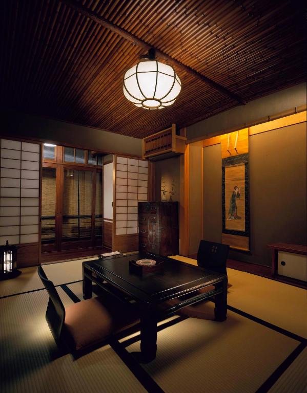 7 UNIQUE Ryokans in Gion Kyoto 21 A traditional Japanese room inspired by ryokans in Gion Kyoto, with tatami mats, shoji screens, a low black table and floor chairs, soft lighting, a hanging lantern, and wall scroll art. Wooden ceiling and decor create a calm, serene atmosphere.