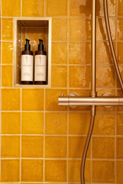 Unique Boutique Hotels in Salzburg 10 A shower with glossy yellow tiles, like those found in boutique hotels in Salzburg, features a brushed metal fixture and a built-in niche holding two brown pump bottles with white labels.