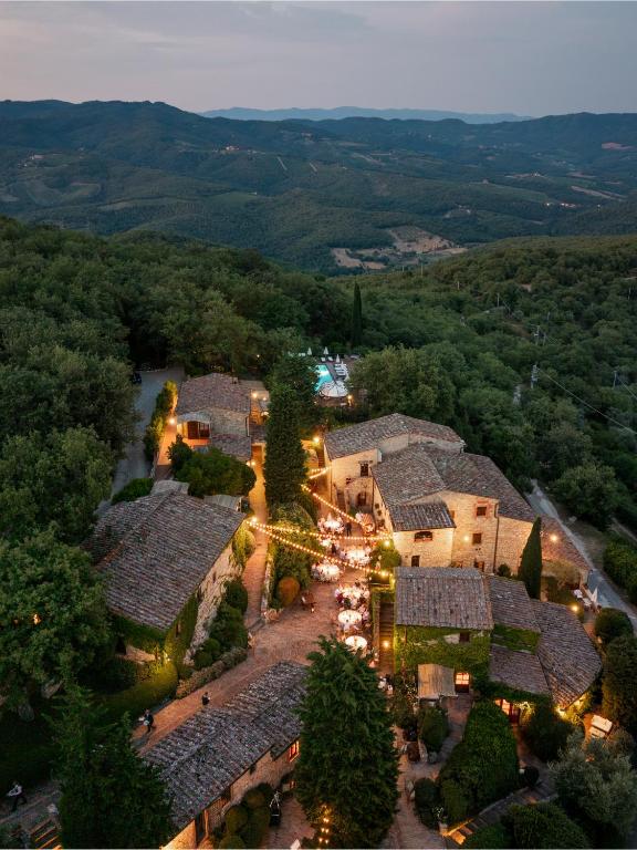 7 Best Agriturismos in Tuscany 27 Aerial view of a rustic stone village nestled among dense green trees, warmly lit at dusk, with people gathered for an event—evoking the charm of agriturismos in Tuscany. Rolling hills and mountains stretch under a soft evening sky.