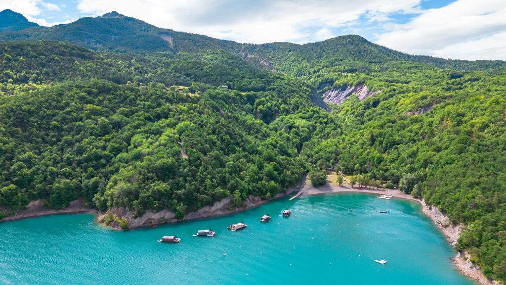 11 Unique Places to Stay in Provence 20 Aerial view of turquoise water in a small bay surrounded by lush green forested hills; several boats are anchored near the shore under a partly cloudy sky, evoking the charm of unique places to stay in Provence.