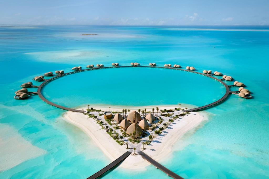 9 Best Hotels in Saudi Arabia: Unique Stays Across the Country 30 Aerial view of a circular luxury resort with overwater villas connected by walkways, surrounding a small sandy island with turquoise water in the Maldives—an experience rivaling the Best Hotels in Saudi Arabia.