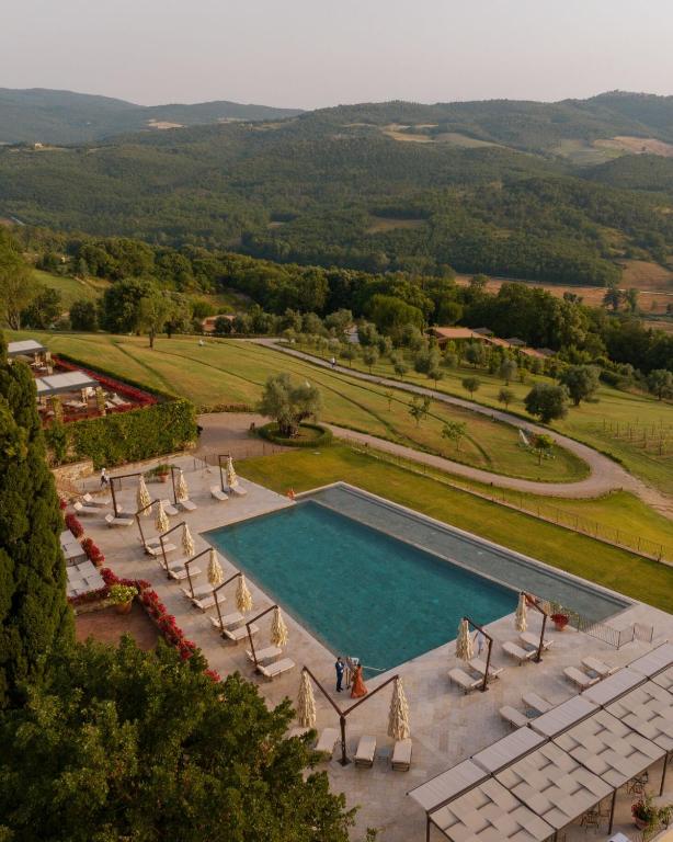 7 Best Agriturismos in Tuscany 14 A rectangular outdoor pool at one of the finest agriturismos in Tuscany is surrounded by lounge chairs and umbrellas, overlooking a lush, green hilly landscape and winding paths, with two people standing poolside.