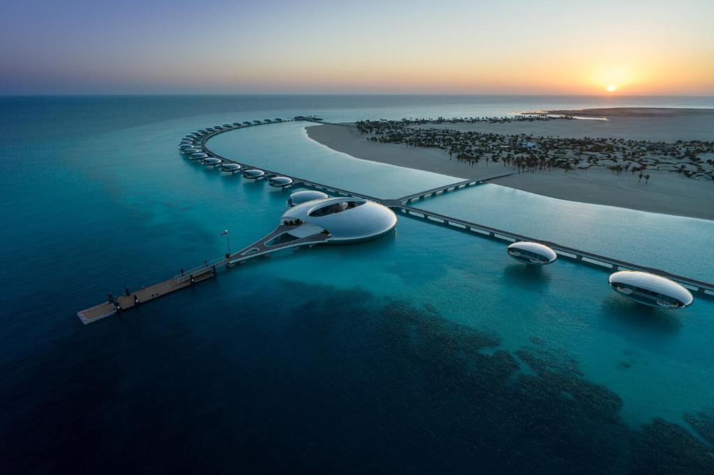 9 Best Hotels in Saudi Arabia: Unique Stays Across the Country 34 Aerial view of a futuristic, circular resort with domed buildings over turquoise water, connected by walkways on a sandy coastline at sunset—one of the best hotels in Saudi Arabia for luxury and innovation.