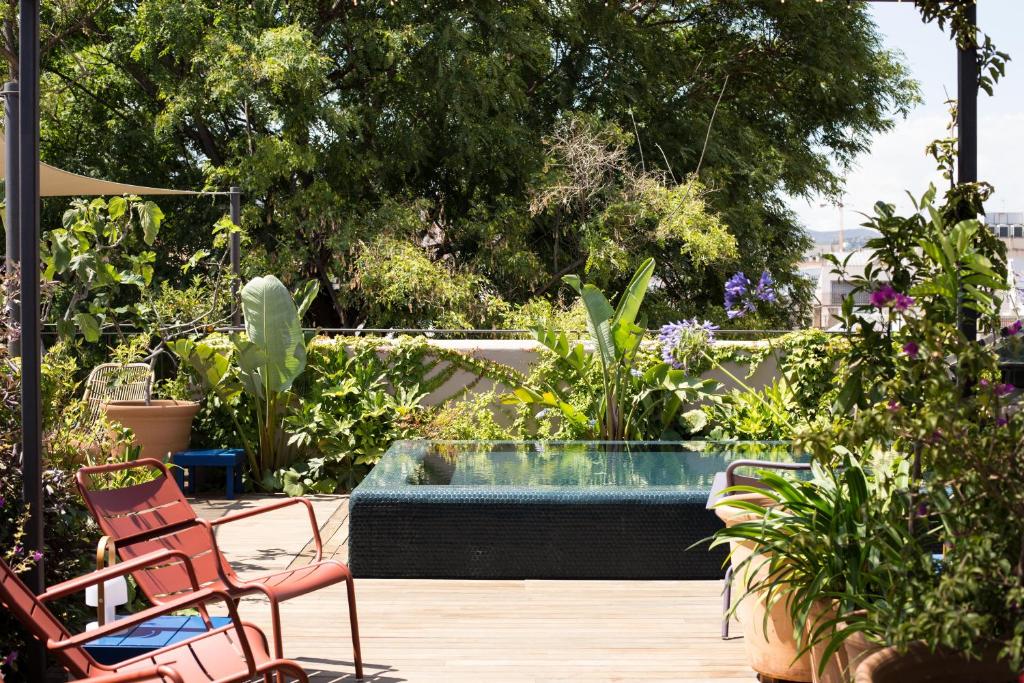 13 Unique Hotels in Barcelona, Spain 45 A small square plunge pool sits on a wooden deck surrounded by lush green plants and trees, with red chairs and potted plants nearby, reminiscent of the tranquil settings found in Barcelona Hotels with Rooftop Pool amenities.