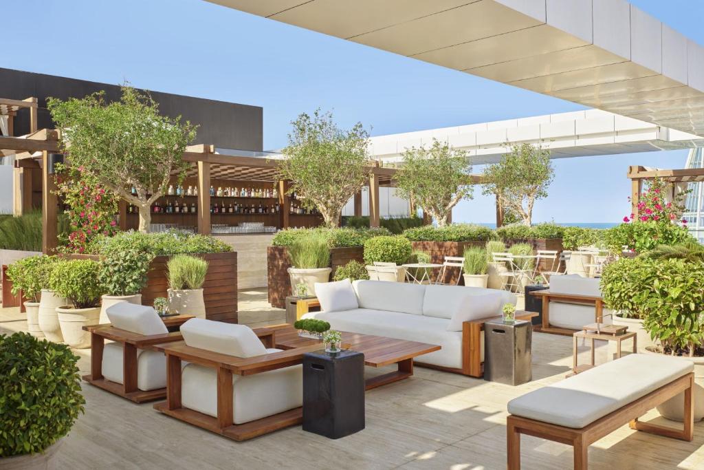 9 Best Hotels in Saudi Arabia: Unique Stays Across the Country 8 A modern rooftop lounge at one of the Best Hotels in Saudi Arabia, featuring white cushioned seating, wooden tables, potted plants, and a bar under a pergola set against a clear blue sky.