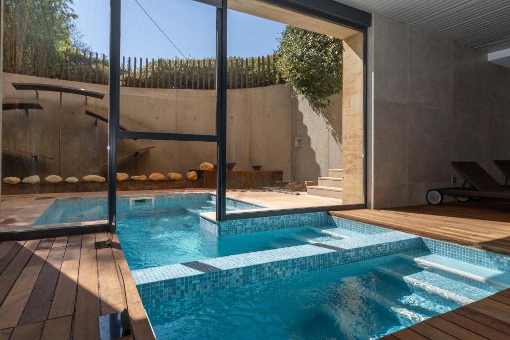 Indoor pool with blue mosaic tiles and wooden deck, extending outdoors through large glass doors. Sunlight streams in, and outside a small patio awaits—reminiscent of the tranquil escapes found at boutique hotels in Asturias.