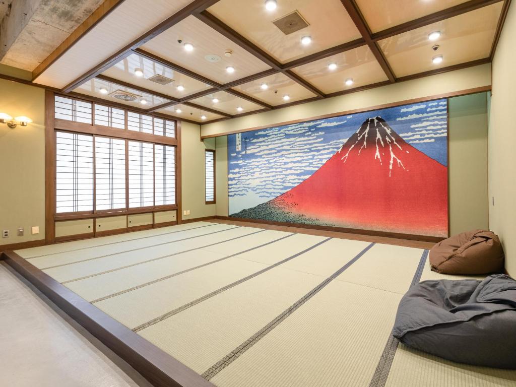 8 BEST Ryokans in Osaka 20 A spacious Japanese-style room inspired by ryokans in Osaka, featuring tatami mats, a Mount Fuji mural, wooden ceiling panels, shoji screen windows, and two brown bean bags in the corner.