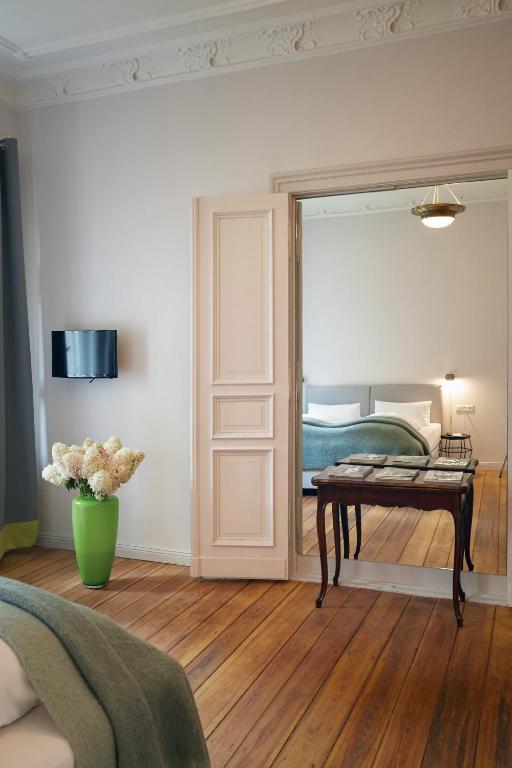 Boutique Hotels in Berlin Kreuzberg 5 A bright room with wooden floors, a small table, and a green vase of white flowers; an open door reveals a cozy bedroomāan inviting scene, much like those found in boutique hotels in Berlin Kreuzberg.
