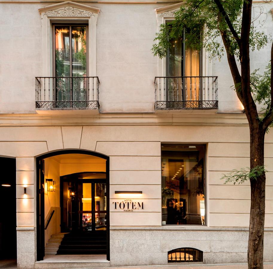 Where to Stay in Madrid: 14 Best Hotels 55 The entrance of a stylish, cream-colored building with black railings and large windows—an inviting option for those wondering where to stay in Madrid first time. A sign reads TOTEM above the door, and a tree partially frames the right side of the image.