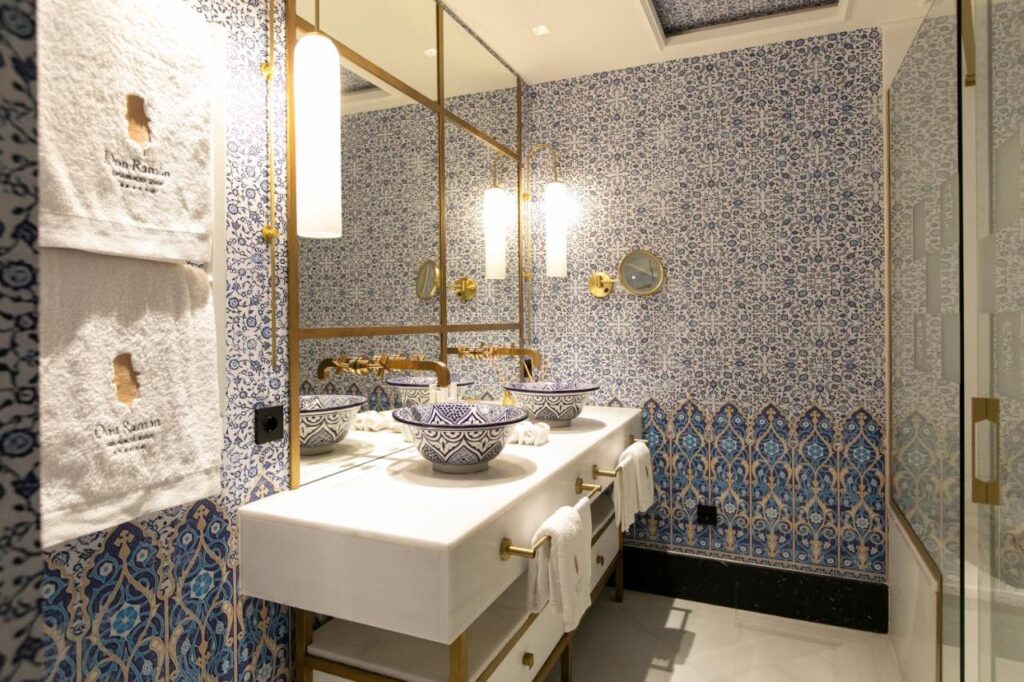 10 UNIQUE Hotels with Pool in Seville 20 Elegant bathroom with intricate blue and white patterned tiles, a double sink with ornate bowls, gold fixtures, and modern hanging lights—perfect for guests seeking hotels with pool in Seville who appreciate luxurious and stylish surroundings.
