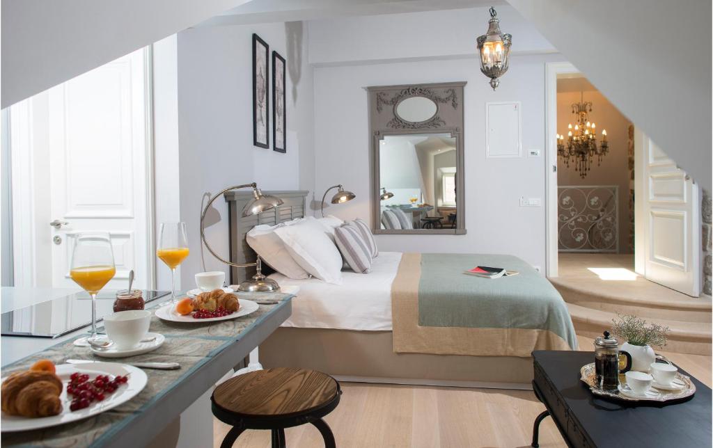 Most Unique Boutique Hotels in Dubrovnik 31 A cozy, elegant bedroom inspired by boutique hotels in Dubrovnik features a neatly made bed, breakfast with pastries and juice on a table, a large mirror above the bed, bright white walls, and an open door revealing a lit chandelier next door.
