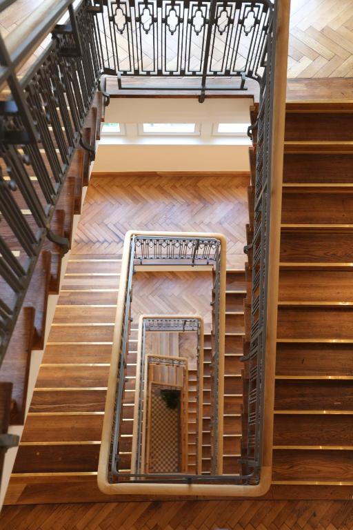 Boutique Hotels in Berlin Kreuzberg 13 A top-down view of a wooden staircase with metal railings, forming a geometric spiral patternāreminiscent of the elegant interiors found in boutique hotels in Berlin Kreuzberg. Sunlight streams in through windows at the top of the image.
