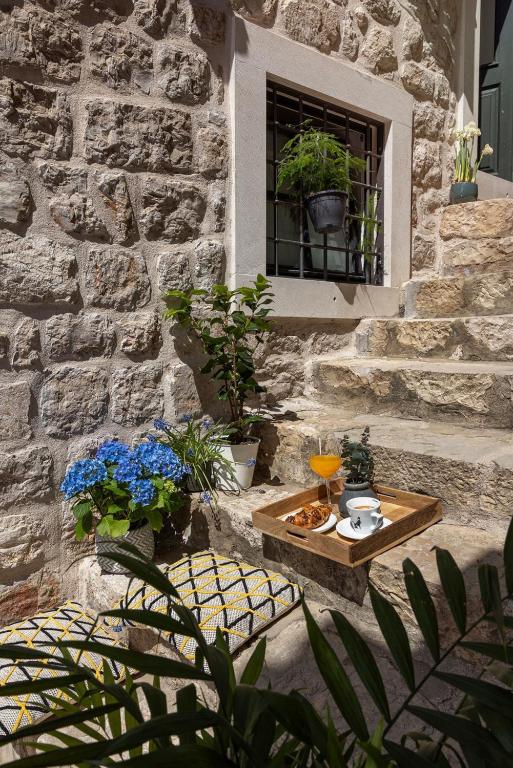 Most Unique Boutique Hotels in Dubrovnik 29 A rustic stone staircase, like those found at boutique hotels in Dubrovnik, holds a tray with coffee, juice, and pastries. Blue hydrangeas, lush plants, and patterned cushions bring color to the cozy scene as sunlight warms the textured wall.