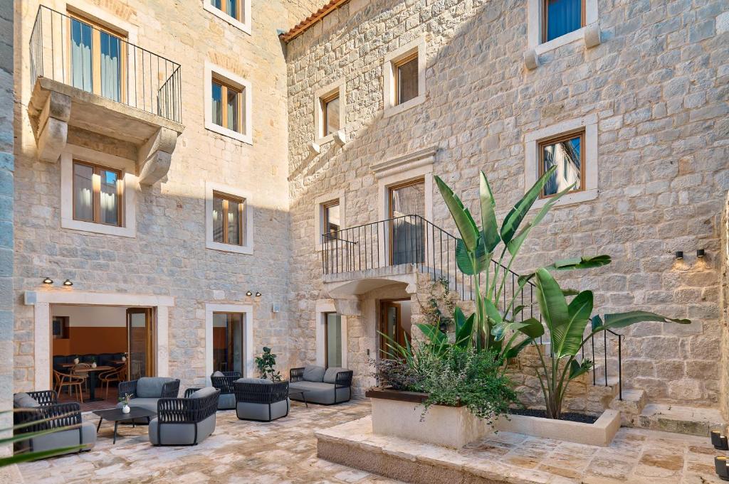 8 TOP Boutique Hotels in Split 16 Sunny stone courtyard with modern outdoor seating, potted plants, and tall green leaves. Perfect for those searching Where to Stay in Split, this building blends historic charm and contemporary style with stone walls, windows, and small balconies.