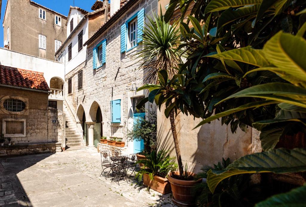 Where to Stay in Split: Hotel & Areas Guide 25 A sunny courtyard with stone buildings, blue shutters, potted plants, and a cozy table and chairs—perfect inspiration when searching for where to stay in Split. An exterior staircase winds up to the inviting upper floor.