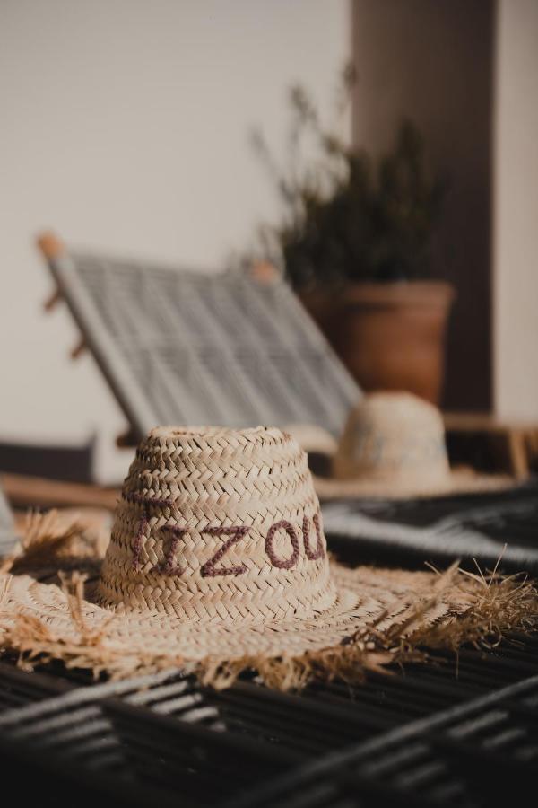12 Charming Budget Riads in Marrakech 29 A woven straw hat with partially visible text rests on a sunlit surface, next to another hat and a blurred reclining wooden chair. A potted plant evokes the relaxed charm of budget riads in Marrakech.