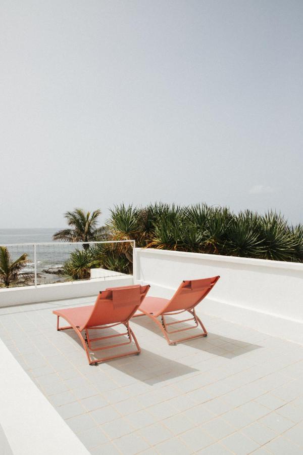 11 UNIQUE Boutique Hotels in Tenerife 10 Two orange lounge chairs sit on a white rooftop terrace at one of the boutique hotels in Tenerife, overlooking the ocean with palm trees and greenery in the background under a clear sky.