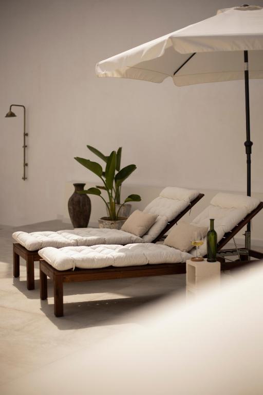 11 UNIQUE Boutique Hotels in Tenerife 14 Two cushioned lounge chairs with pillows sit under a large white umbrella on a sunlit patio, evoking the relaxed luxury of Boutique Hotels in Tenerife. Nearby are a potted plant, decorative vase, small table with wine bottle, and a glass.