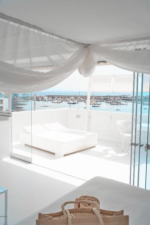 Adults Only Hotels in Fuerteventura 22 A bright, modern room with white furniture and sheer curtains overlooks a marina filled with boats. Sunlight pours in through large glass windows, creating a serene and airy atmosphere typical of adults only hotels in Fuerteventura.