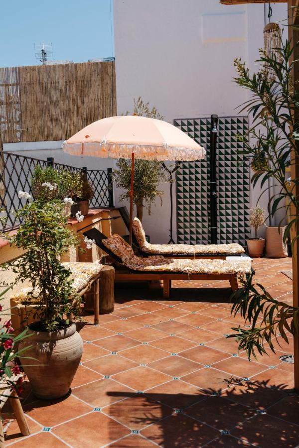 Where to Stay in Madrid: 14 Best Hotels 40 A sunny patio with terracotta tiles, two cushioned lounge chairs under a peach umbrella, potted plants, and rustic wooden furniture—this is the perfect spot for anyone seeking where to stay in Madrid first time, set against white and bamboo fencing.