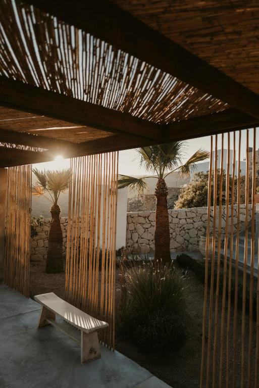 11 UNIQUE Boutique Hotels in Tenerife 6 A modern outdoor patio with a wooden slatted roof and vertical bamboo poles, a simple bench, palm trees, and a stone wall—all bathed in warm sunset light—echoes the serene style of boutique hotels in Tenerife.