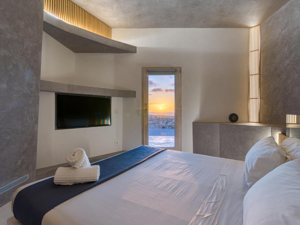 Adults Only Hotels in Fuerteventura 8 Modern hotel room with a neatly made bed, rolled towels, wall-mounted TV, and minimalist décor. A door opens to a view of the sea and a colorful sunset sky—perfect for those seeking adults only hotels in Fuerteventura.