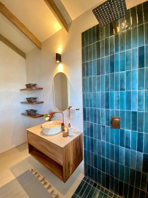 8 UNIQUE Places Where to Stay in Lake Atitlán 29 Modern bathroom with blue tiled shower, wooden floating vanity and vessel sink—just the style you’ll find when searching where to stay in Lake Atitlan. Features include an oval mirror, open shelves with baskets, soft lighting, and exposed wooden ceiling beams.