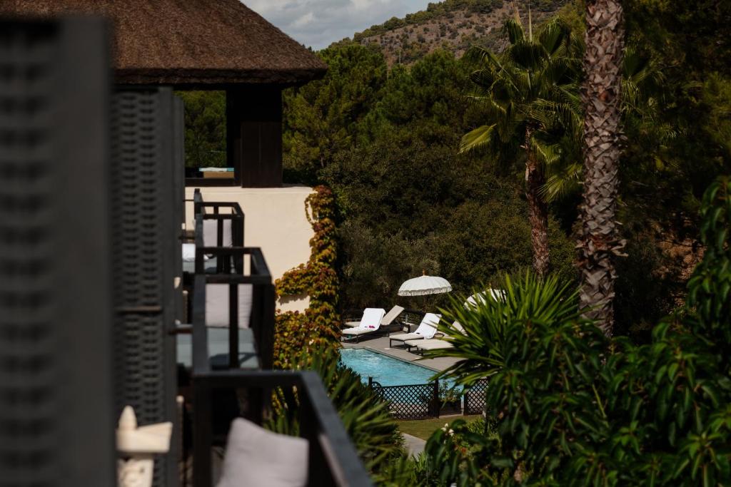 Adults-Only Hotels in Costa del Sol 26 A view of a swimming pool surrounded by lounge chairs and lush greenery, with palm trees and hills in the background, partially seen through the balconies of a nearby building at one of the adult only hotels in Costa del Sol.