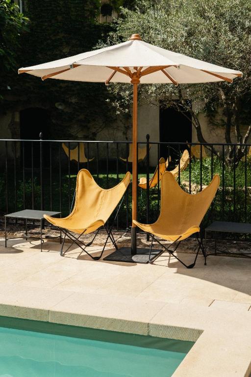11 Unique Places to Stay in Provence 11 Two yellow butterfly chairs sit under a white patio umbrella beside a pool, with greenery and a black iron fence in the background—one of the unique places to stay in Provence.