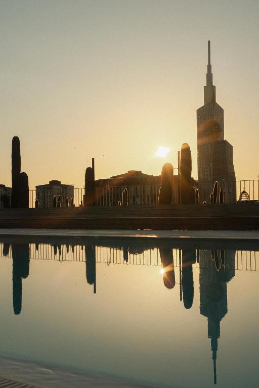 11 Unique Hotels in Georgia You Can't Miss! 41 The sun sets behind a city skyline with a tall, modern buildingāreminiscent of unique hotels in Georgiaāand several silhouettes of cacti, all reflected in a calm pool of water in the foreground.