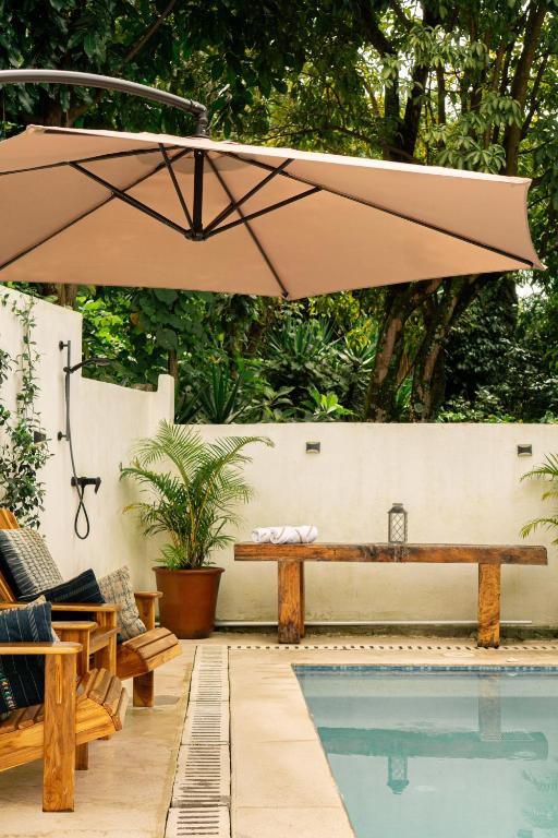 8 UNIQUE Places Where to Stay in Lake Atitlán 20 Outdoor shower area beside a pool with lounge chairs under a tan umbrella, a wooden bench with a towel and lantern, and lush greenery—perfect inspiration for where to stay in Lake Atitlan.