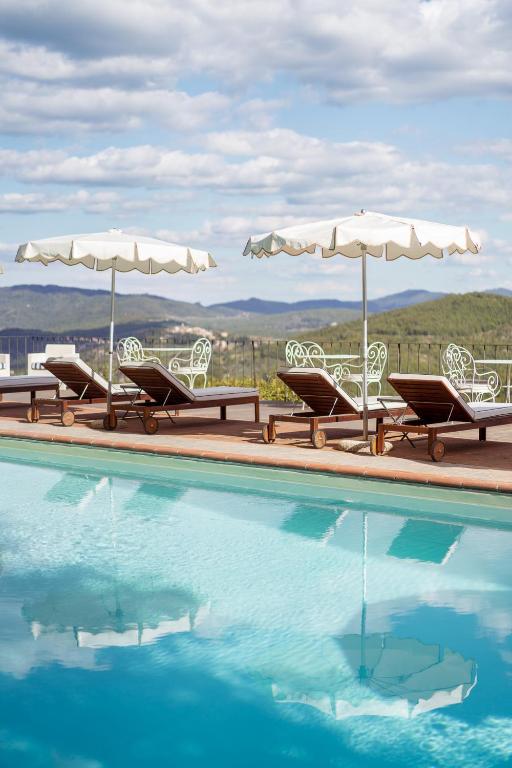 7 Best Agriturismos in Tuscany 26 A swimming pool with lounge chairs and white umbrellas beside it, overlooking a scenic landscape of green hills under a partly cloudy sky—perfect for relaxing at one of the charming agriturismos in Tuscany.