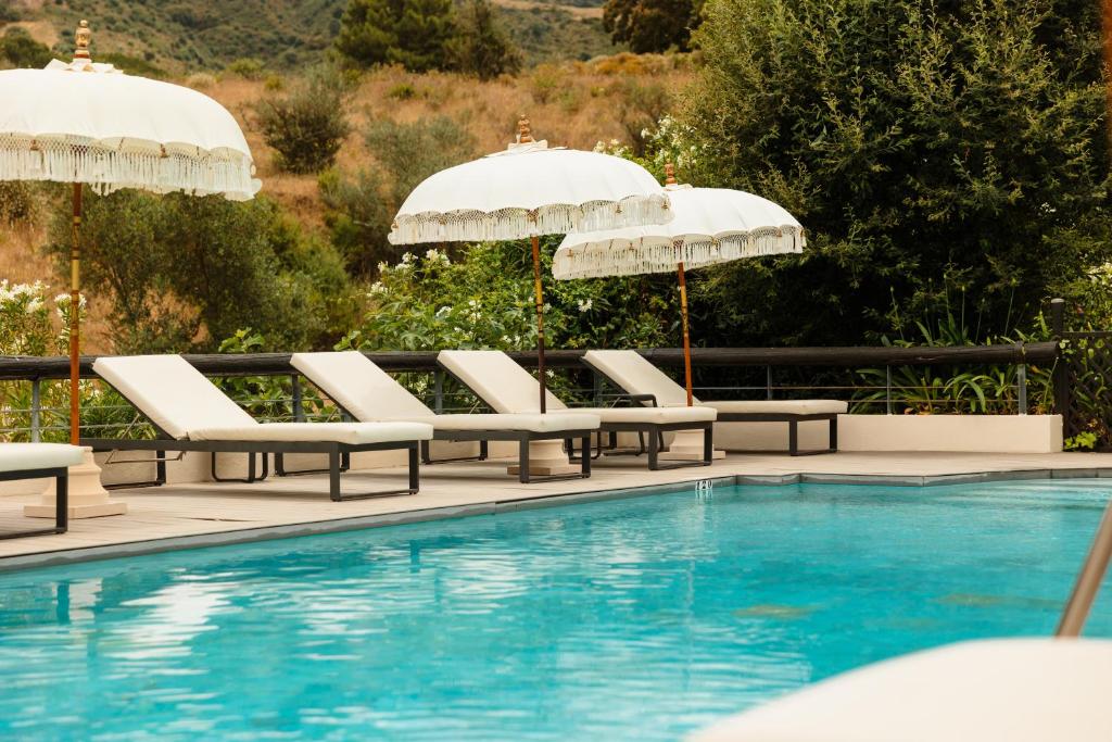Adults-Only Hotels in Costa del Sol 24 Several white lounge chairs and large umbrellas line the edge of a clear blue swimming pool, surrounded by lush greenery—a tranquil scene often found at adult only hotels in Costa del Sol.