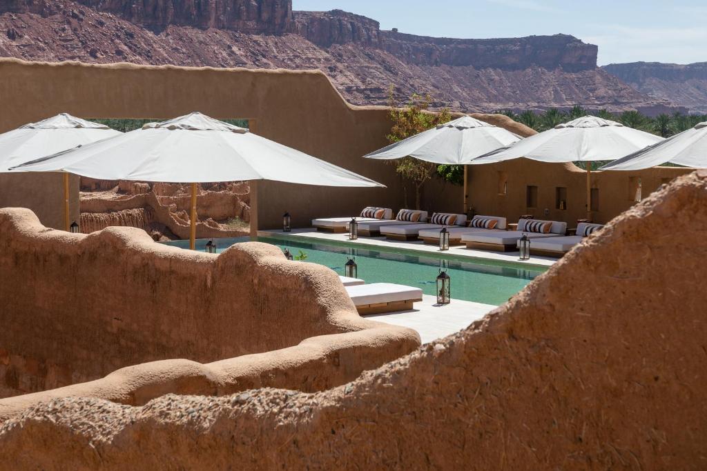 9 Best Hotels in Saudi Arabia: Unique Stays Across the Country 18 Experience one of the Best Hotels in Saudi Arabia with an outdoor pool area framed by adobe-style walls, striped lounge chairs, and large white umbrellas, all set against breathtaking rocky desert cliffs and a clear sky.